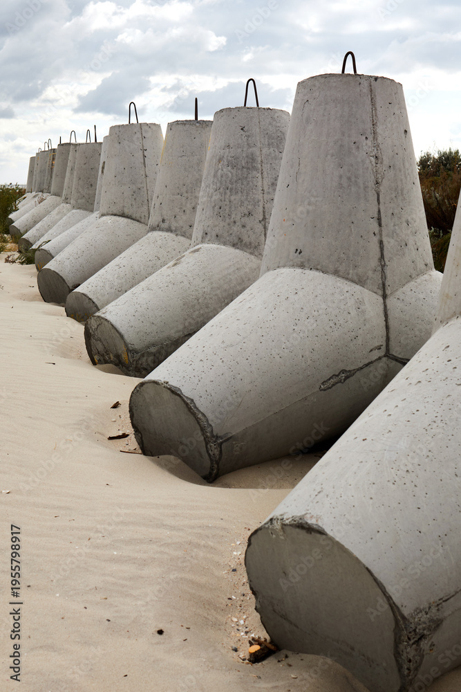 Fototapeta premium Concrete coastal barriers lined along sandy beach under cloudy dramatic sky