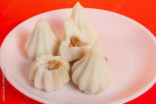 Steamed sweet modak rice dumplings on a white plate against a bright red background