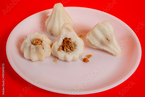 Steamed sweet modak rice dumplings on a white plate against a red background for the Ganesh Chaturthi festival.