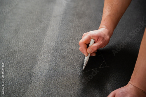 Close up of man drawing cutting guide lines on black flooring underlay with white marker while preparing material for linoleum installation during renovation