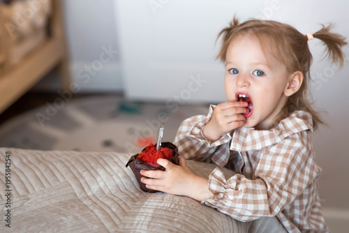 Tableau sur toile A little girl of 2 years old with a muffin or cupcake with a candle in a home environment