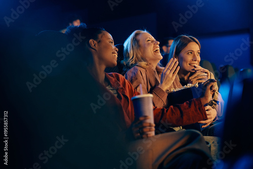 Happy woman laughing while watching comedy film with her friends at movie theater.