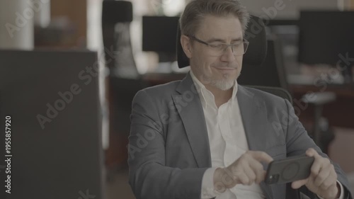 Business portrait - confident businessman sitting at desk working in office, using phone. Happy mid adult man in shirt and jacket, smiling. Video in LOG format - S-LOG3 Cine.