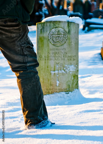 A person standing in the snow next to the grave of S. Boulton, a soldier from the Gloucestershire Regiment.