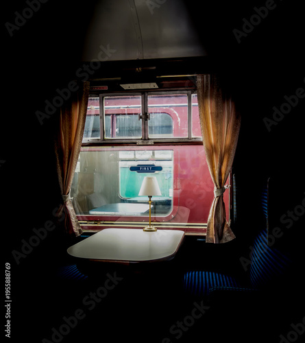 Interior of a vintage train car with a table, lamp, and window.