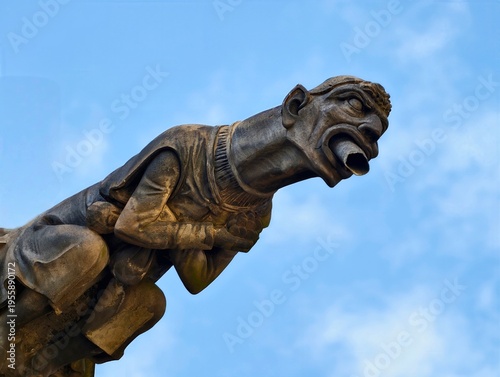 Weathered carved stone gargoyle jutting from roof edge showcasing open mouth and expressive features