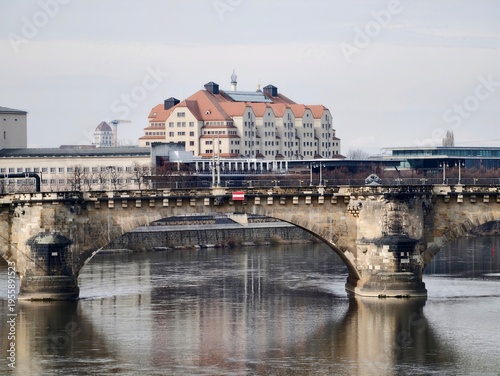Timeless stone bridge stretching across serene water with nearby city skyline and subtle figures