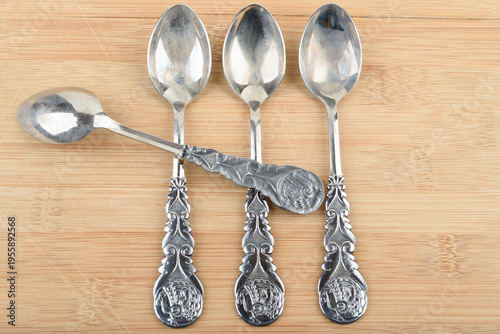 Vintage silver plated teaspoons with intricate patterns on wood.