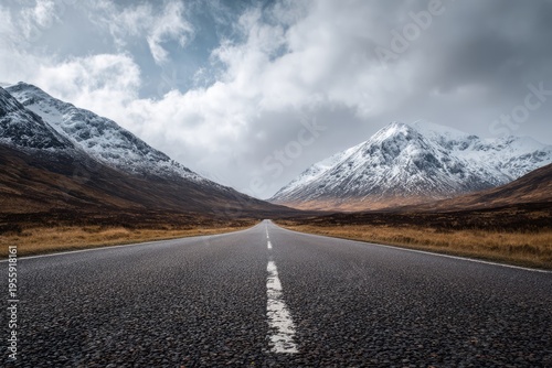 Scenic Road Through Snowy Mountains Under Cloudy Sky.