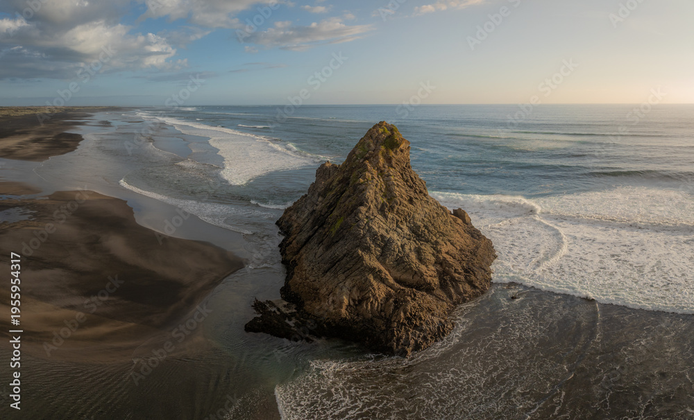 Naklejka premium Aerial view of the iconic Rock at Karekare Beach, New Zealand. Waves crash around the rock formation, showcasing the rugged beauty of the coastline in Auckland.