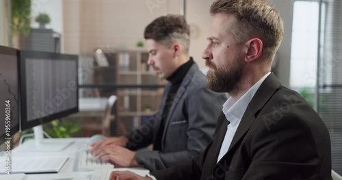 Businessman analyst at computer in office accounting report. Two colleagues analyze reports on dual screens, showing teamwork and analytics for budgeting, balance. Finance team plans for wise plans.