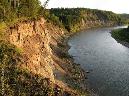 A wide river flows along a steep, eroded cliff face covered in trees and vegetation.