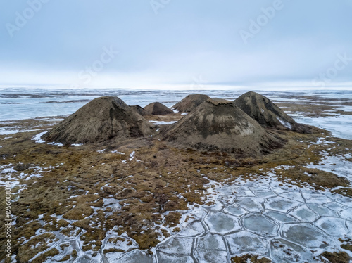 Mud volcanoes in the Arctic tundra landscape during winter with frozen ground and ice formations.
