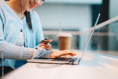 Young adult gen Z woman typing password on laptop keyboard hand holding credit card shopping online relax at cafe