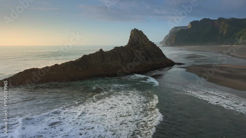 A scenic view of Karekare Beach, New Zealand, showcasing a Rock, a natural rock formation, as waves crash against the shore, highlighting the area's natural beauty.
