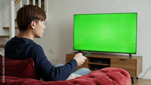 Young man watching movie on LCD TV with green screen for chroma key