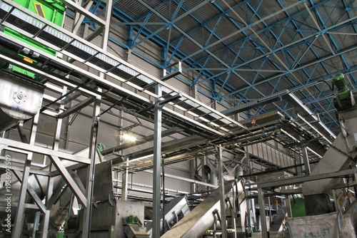 Interior view of a large industrial recycling plant with various complex sorting machines, conveyor belts and metal structures under a blue roof inside a factory warehouse. Works. Technical plant view