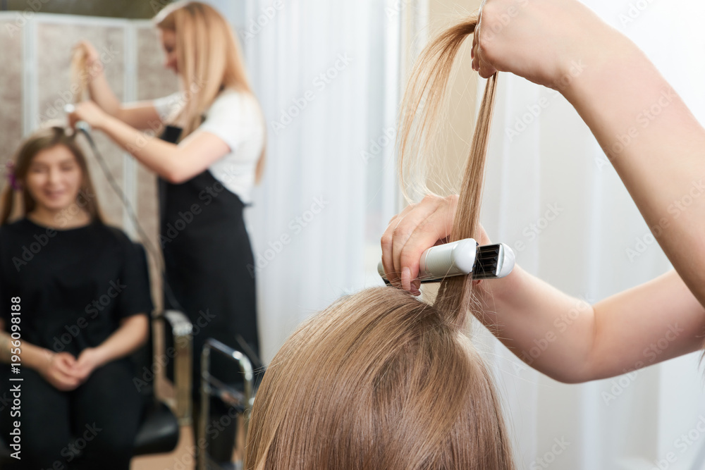 Fototapeta premium Hairstylist working on woman client with crimper