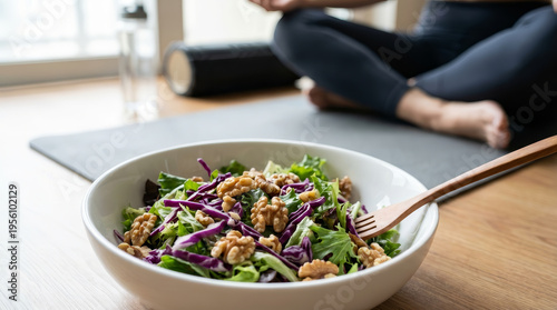 Healthy fresh green salad with walnut and red cabbage in white bowl on wooden floor near blurred person sitting on yoga mat feeling peaceful and relaxed