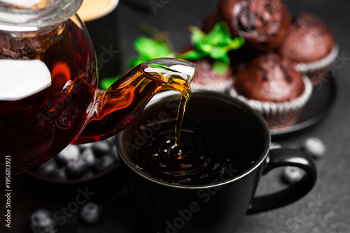 Tea with muffins on a dark background. Chocolate muffins with blueberries. Black tea with mint. High quality photo