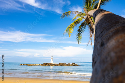 A view of the coconut-lined beach at the lighthouse in Khao Lang, Thailand, against a beautiful sky.