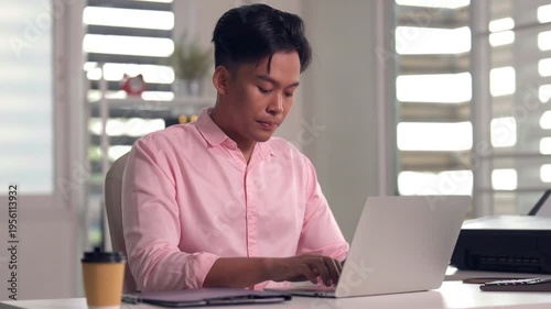 Asian young adult business colleagues review project data on tablet and laptop computer sharing ideas in bright modern office workplace