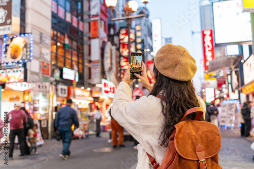 Young female tourist taking a photo of tourist and nightlife areas in Dotonbori district in Osaka, Japan