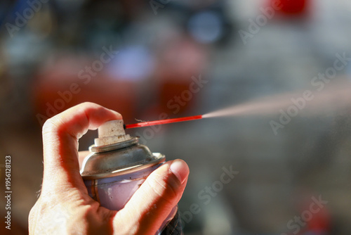 Focused hand pressing an aerosol spray can nozzle, releasing pressurized liquid lubricant in workshop. close up view of maintenance and careful application with tool