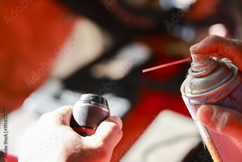 Close up of mechanic hand holding part for maintenance, carefully cleaning with spray lubricant can in red workshop. focused repair work shows great concentration