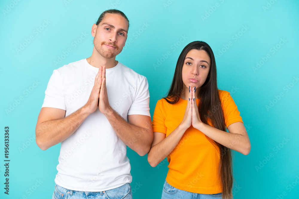 Fototapeta premium Young caucasian couple isolated on blue background pleading
