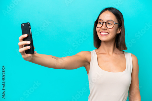Young caucasian woman isolated on blue background making a selfie with mobile phone