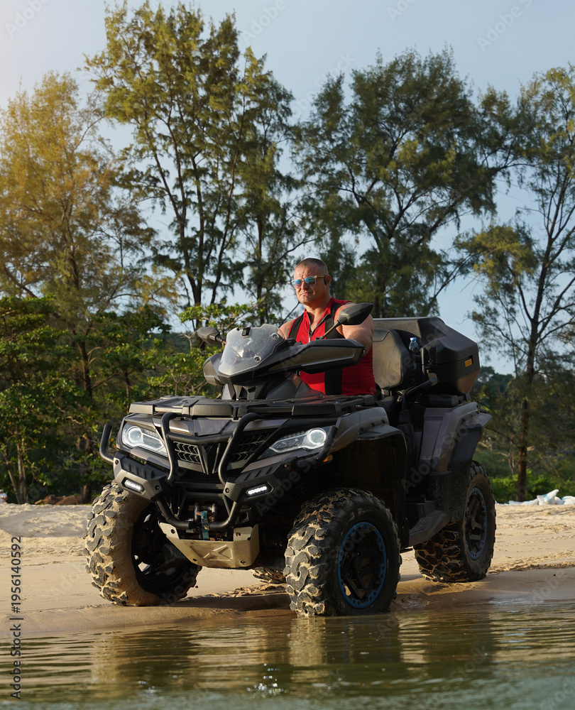 Fototapeta premium A man engages in extreme ATV riding on sand beach early in the morning