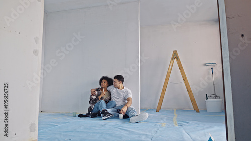 Schilderij op canvas A couple sits on a blue drop cloth in a room under renovation, surrounded by white walls and a wooden stepladder showing intimacy amidst home improvement