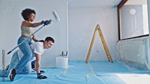 Cuadro en lienzo A joyful couple engages in playful banter during a home renovation project, with one painting and the other playfully wielding a foam roller