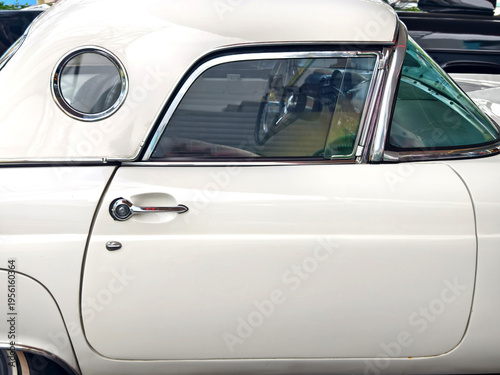 White classic car parked on street, gleaming chrome trim and polished hubcap reflecting sunny urban
