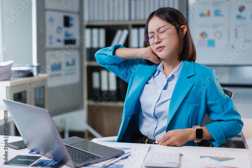 Fotografia Young Asian businesswoman experiencing severe neck pain and discomfort, rubbing