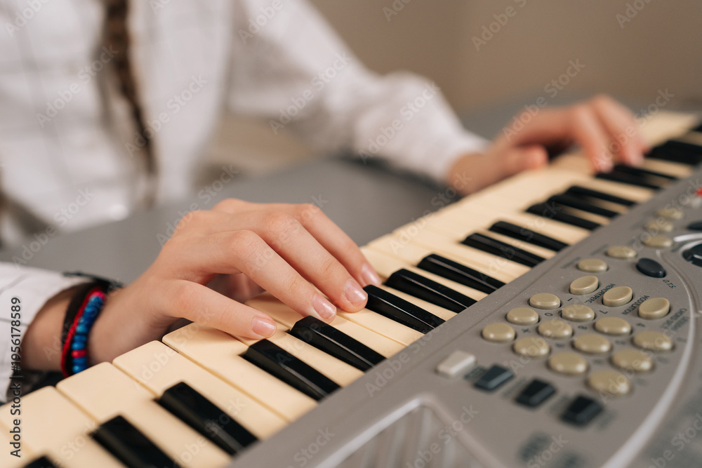 Obraz premium Close-up hands of unrecognizable young girl playing digital piano at home, learning music, practicing keyboard skills, enjoying musical education as hobby