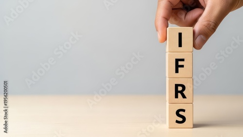 Hand stacks wooden blocks spelling out the acronym ifrs for international financial reporting standards.