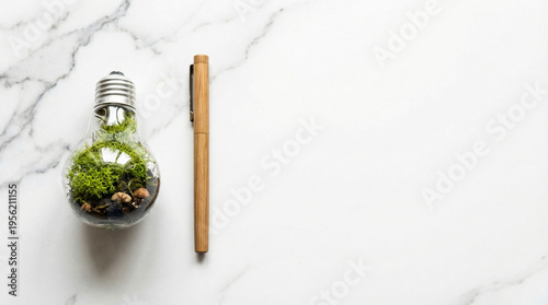 Light bulb terrarium with green moss and a wooden pen on a white marble background. Concept of eco-friendly ideas, green energy, sustainable innovation, and environmental inspiration.