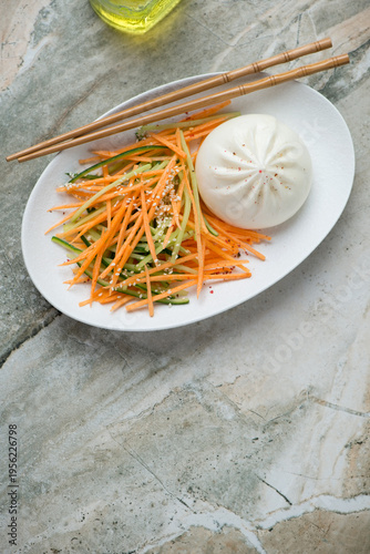 Plate with asian cucumber carrot slaw and steamed bao on a grey granite background, vertical shot with space, above view