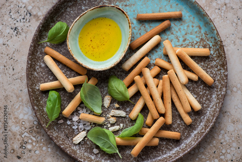Salted breadsticks with olive oil and green basil on a brown plate, horizontal shot, high angle view