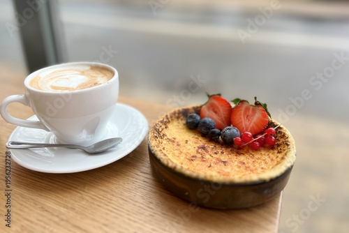 Delicious crème brûlée with crispy caramel top and berry garnish next to a cappuccino, warm natural light, stylish cafe presentation.