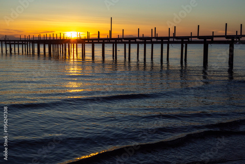 Billede på lærred Dismantled wooden sundeck and pier pilings on a calm sea shore at sunset