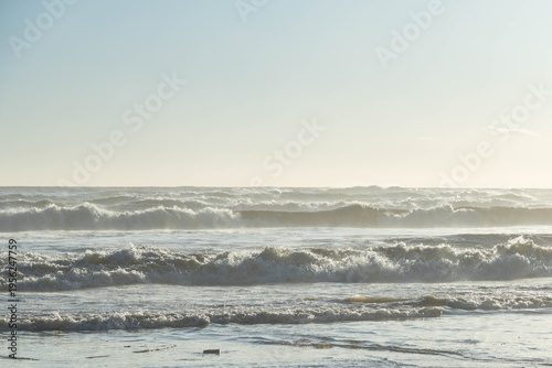 Powerful Mediterranean sea waves rolling onto a sandy beach under a bright evening sky. Scenic coastal landscape with backlight effects and sea spray during the winter low season. Turkey.