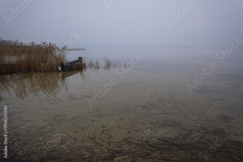 Old rural wooden, fishing boat is moored on the shore of a lake. A gloomy foggy day