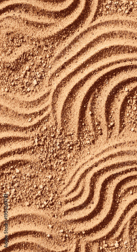 Warm brown sand texture featuring elegant, raked wavy patterns and scattered fine grains, creating a calming and natural abstract background.