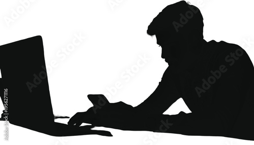 Young man silhouetted while working diligently on a laptop computer and holding a mobile device.