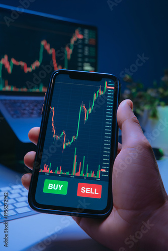 Photography Close-up of a trader hand holds a smartphone with trading app, financial charts or cryptocurrency prices on screen, showing buy and sell buttons during online stock buying or crypto investing