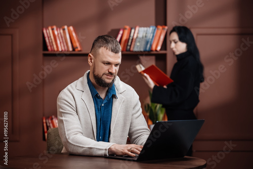 Professional businessman working at desk with woman reading in background. Office work concept.
