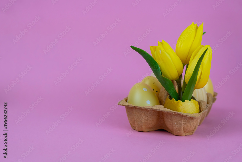 Obraz premium Easter greeting card with yellow tulips in eggshell and decorated eggs in carton on pastel background with copy space